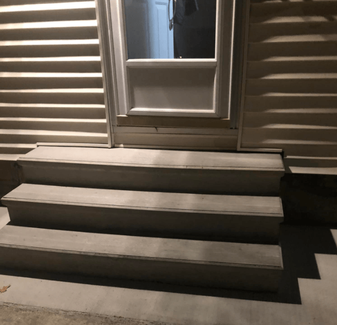 Front porch steps leading to a doorway beside beige siding and a window