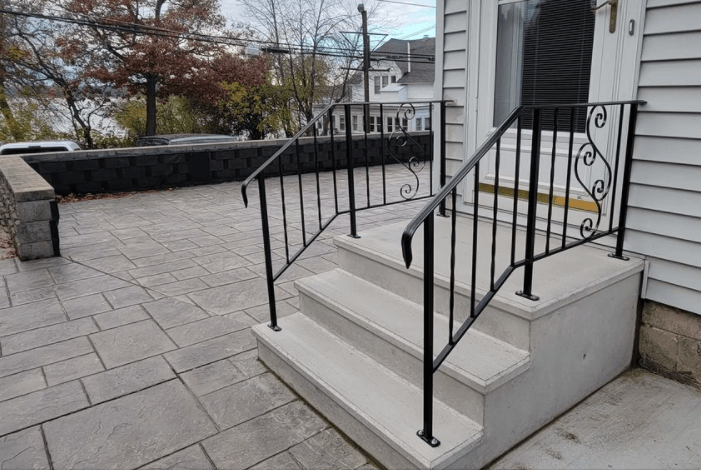 Front steps with black railings leading to a house entrance beside a stone-paved patio