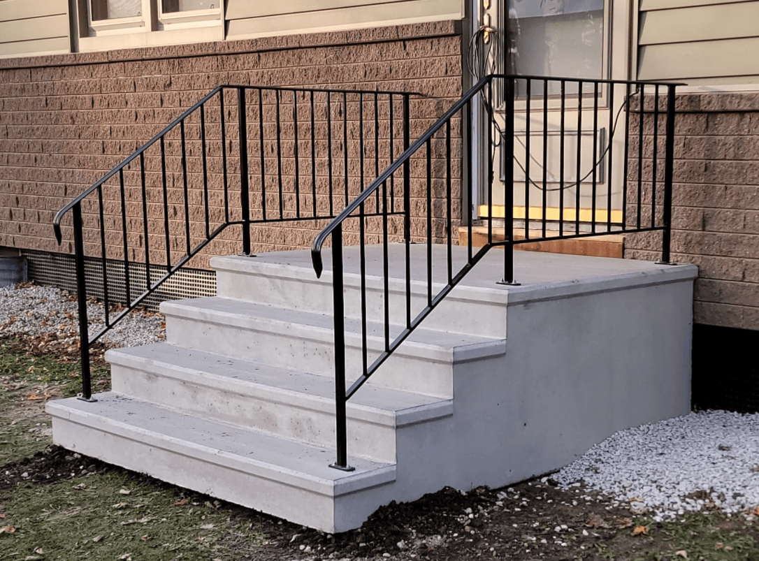 Concrete steps with black metal railings leading to a brick building entrance ramp