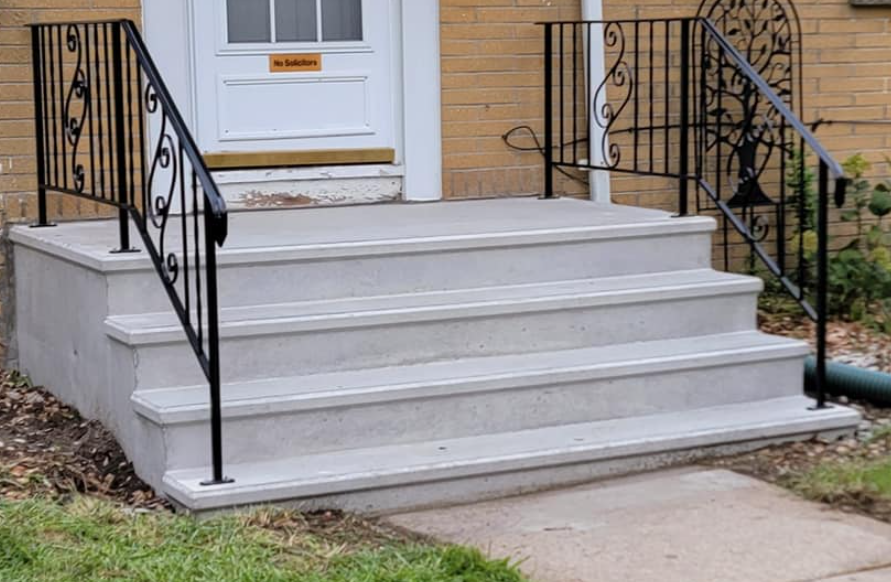 Front porch steps with black iron railings leading to a white door on a tan brick house