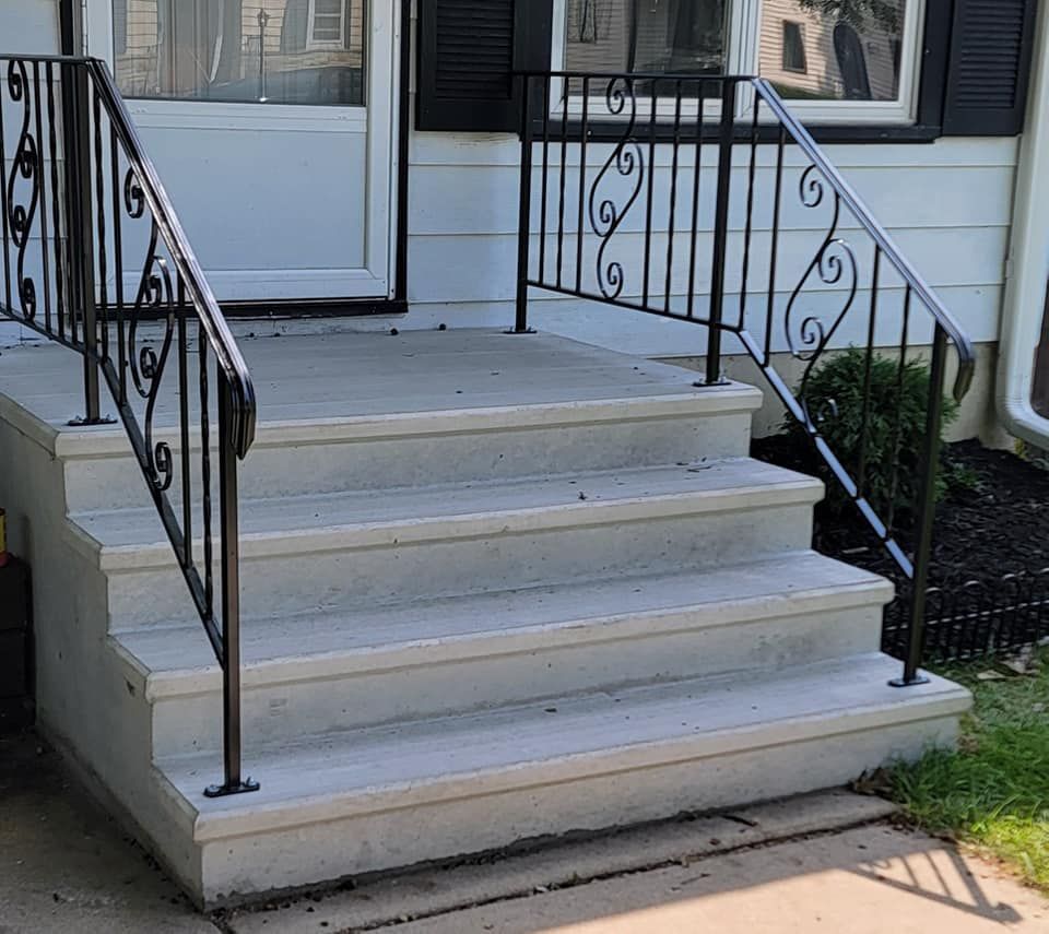 Front steps with black wrought-iron railings leading to a white house entrance