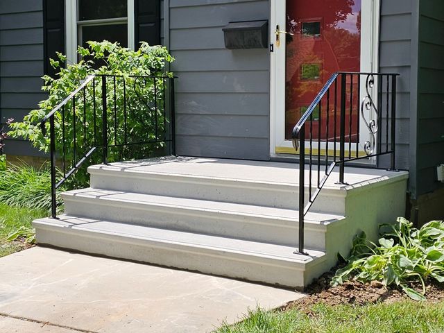 Front steps with black railings leading to a red front door on a gray house