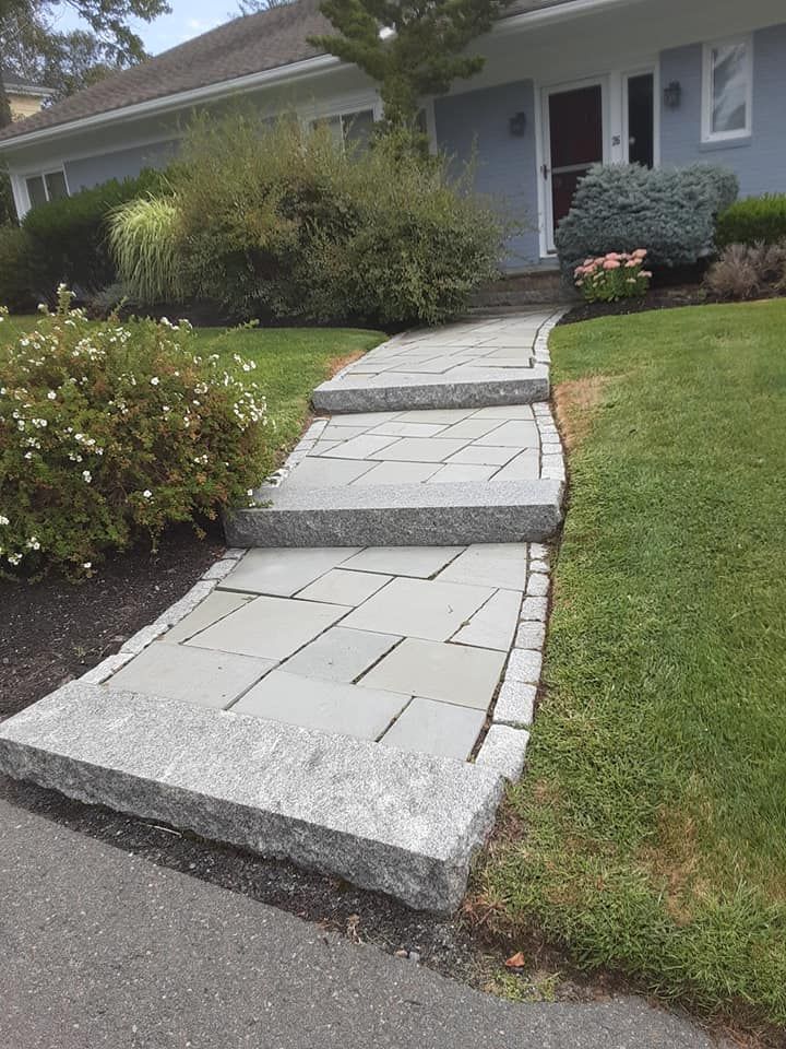 Stone steps leading up to a light blue house entrance, surrounded by green grass and landscaping.