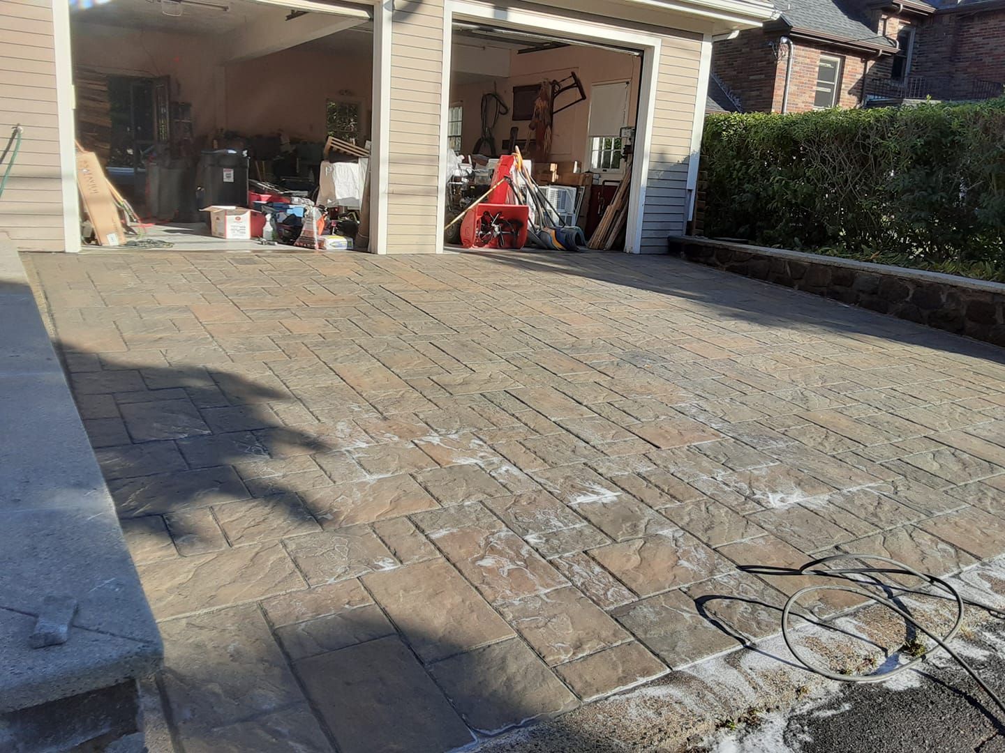 Driveway with patterned pavers leading to a partially open garage filled with items.