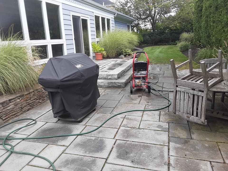 Patio with covered grill, pressure washer, and table; green hose. House in the background.