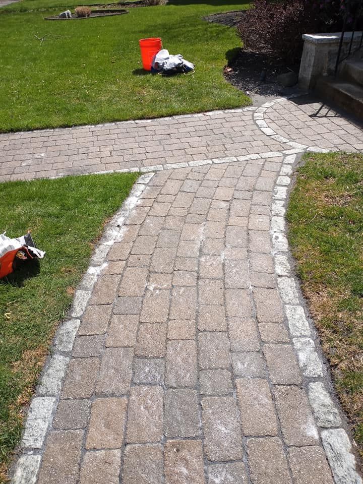 Brick pathway curving through a green lawn, edged with light-colored stones, leading to a front porch.