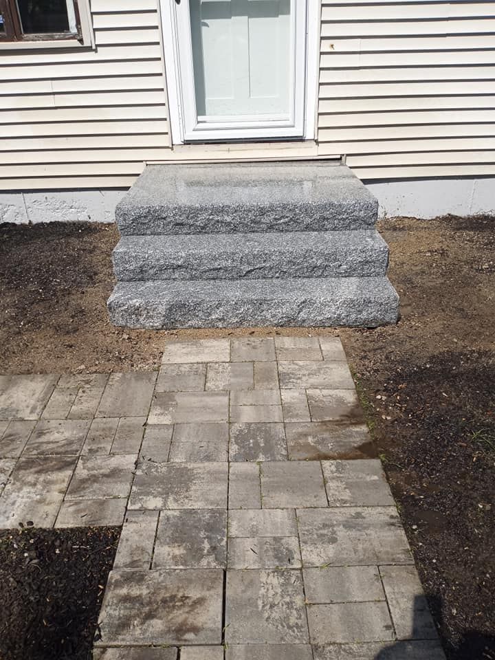 Stone steps leading to a white door, with a paved walkway in front.