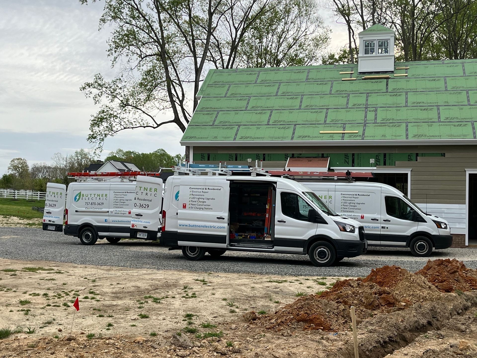 Three white service vans parked near a building under construction, all with open doors.