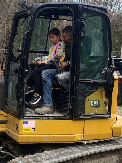 A man and a little girl are sitting in a cat excavator.