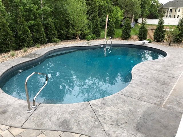 a large swimming pool surrounded by trees and a brick patio .