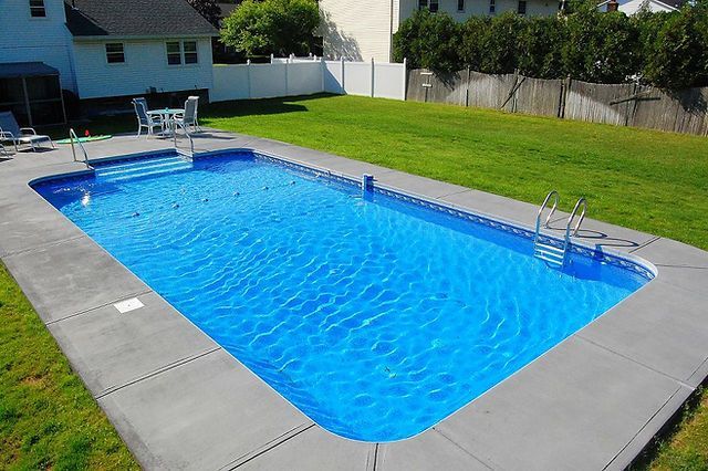 A large swimming pool surrounded by grass and a white fence