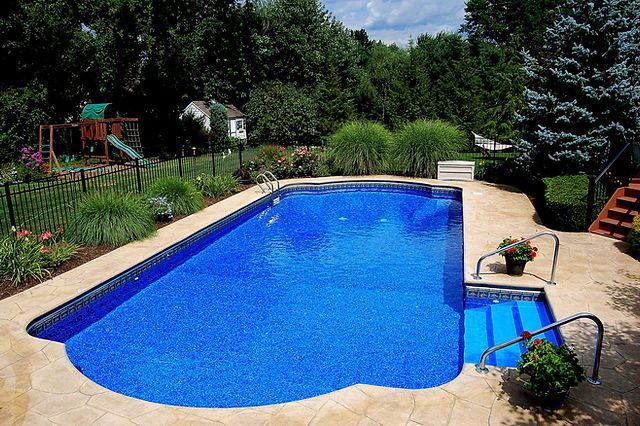 A large blue swimming pool in a backyard with a playground in the background