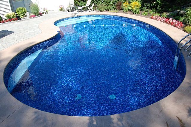A large blue swimming pool with a patio in the background
