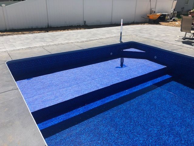 a blue swimming pool with stairs and a fence in the background