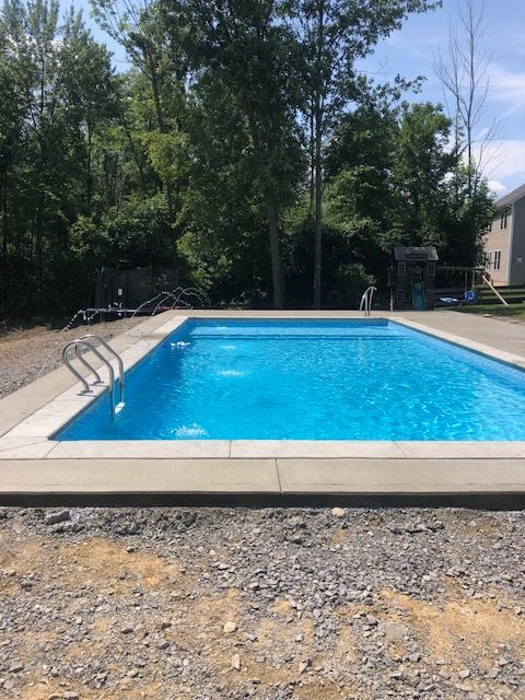 a large swimming pool is surrounded by trees and gravel .