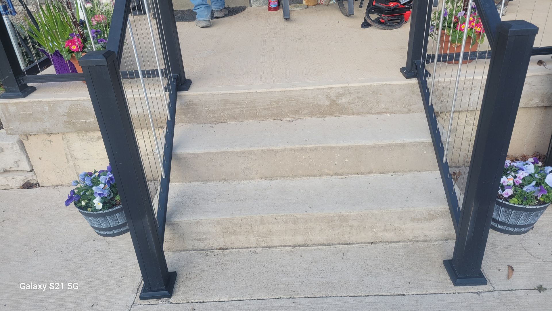 Front steps with black railings and potted flowers leading to a house entrance