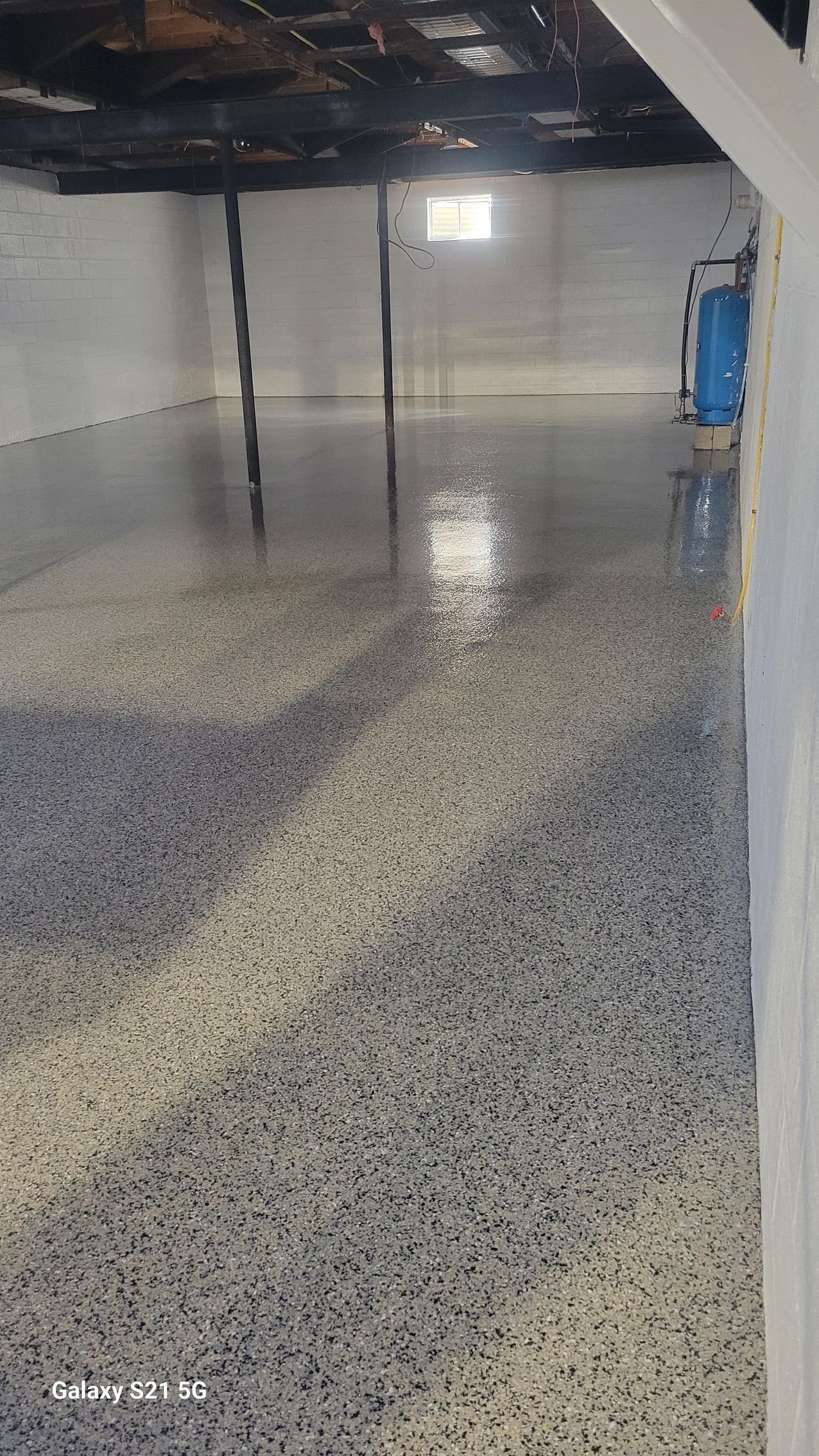 Empty indoor floor with glossy speckled coating, reflected lights, and a blue bin in the background