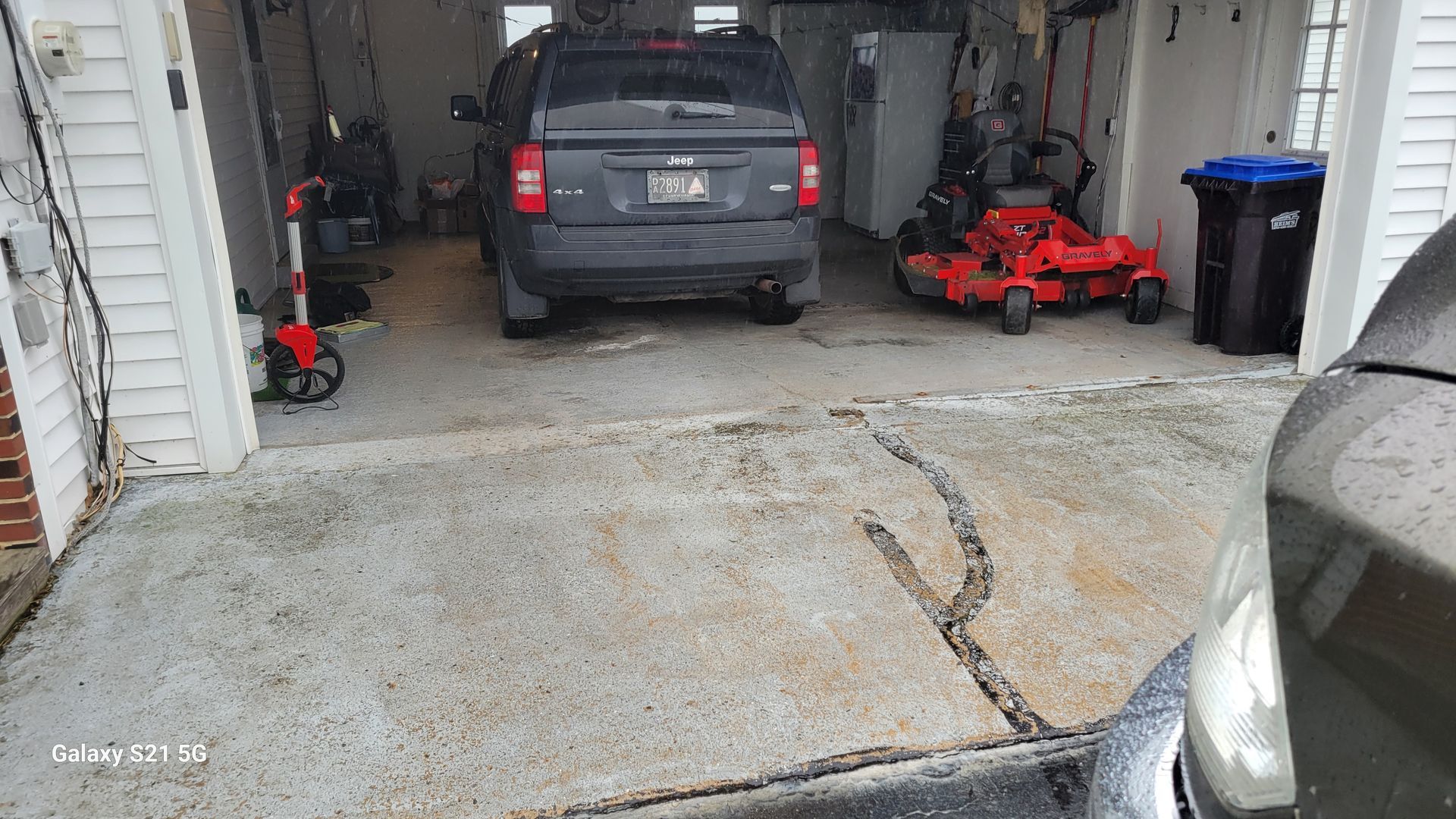 Parked gray SUV in a garage with a red riding mower and concrete floor in front