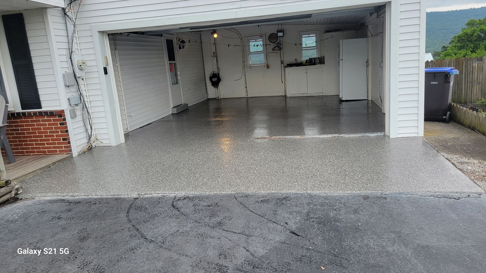Open garage with a polished floor, storage shelves, and a hose on the far wall, viewed from the driveway.