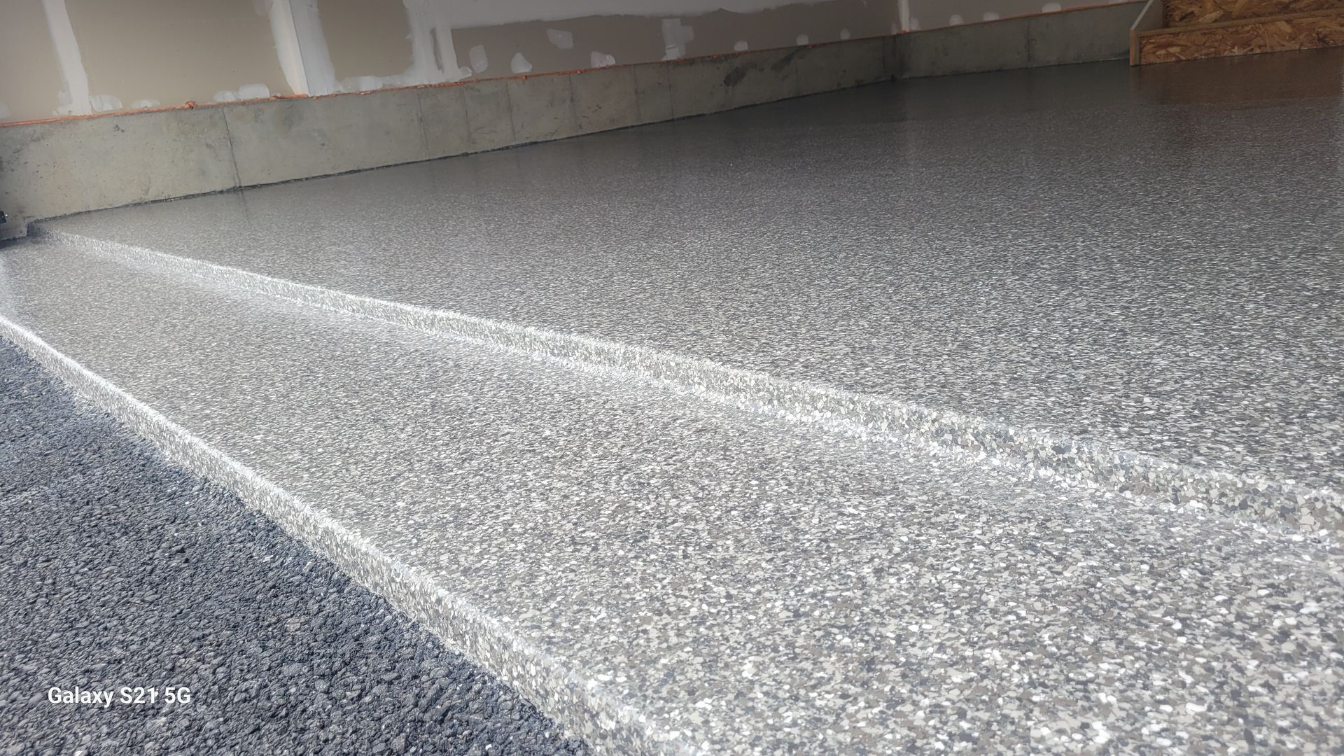 Concrete ramp with a white painted line and rough gray flooring against a wall indoors