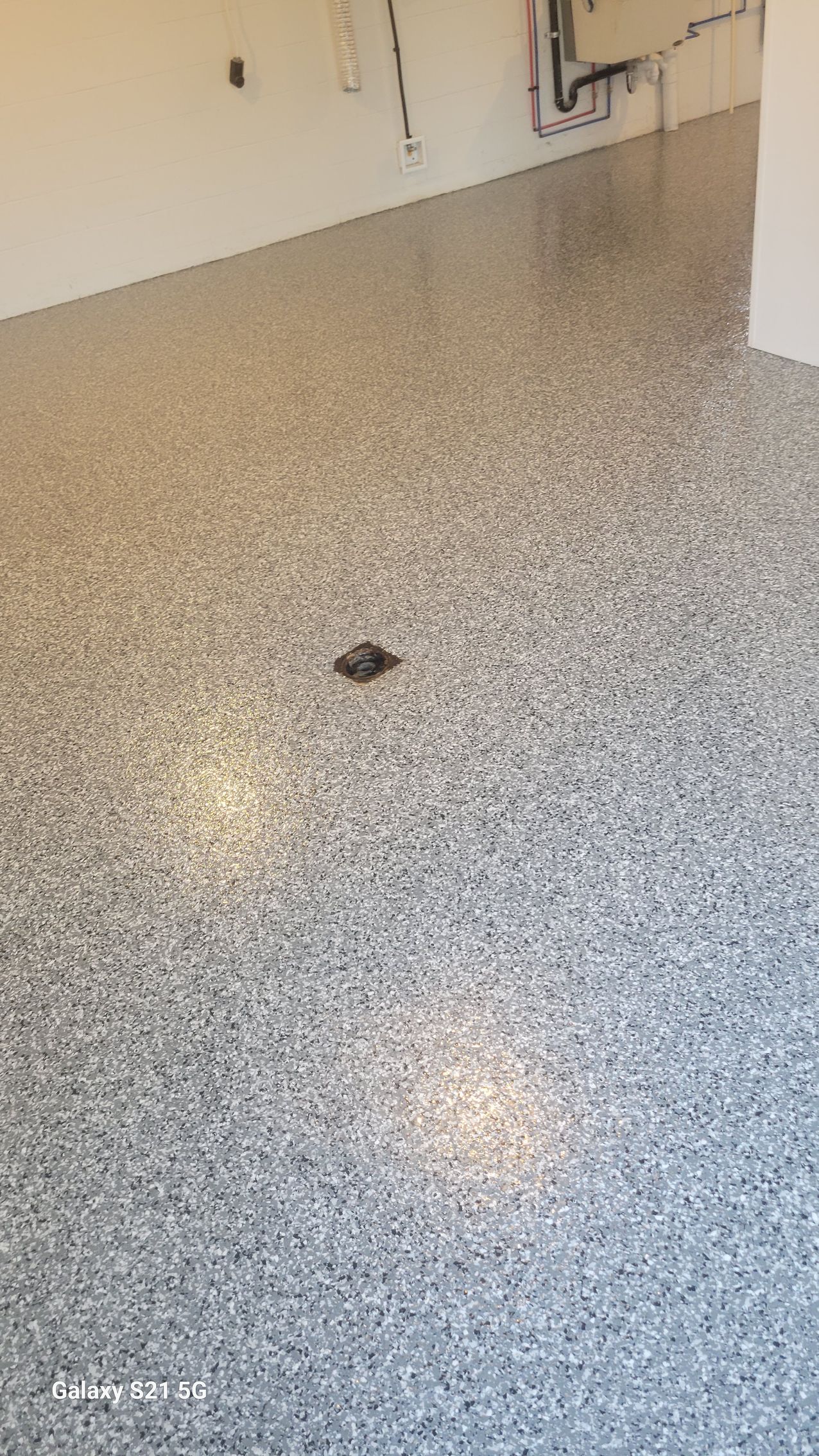 Empty speckled floor with a small square drain near the center and beige walls in the background