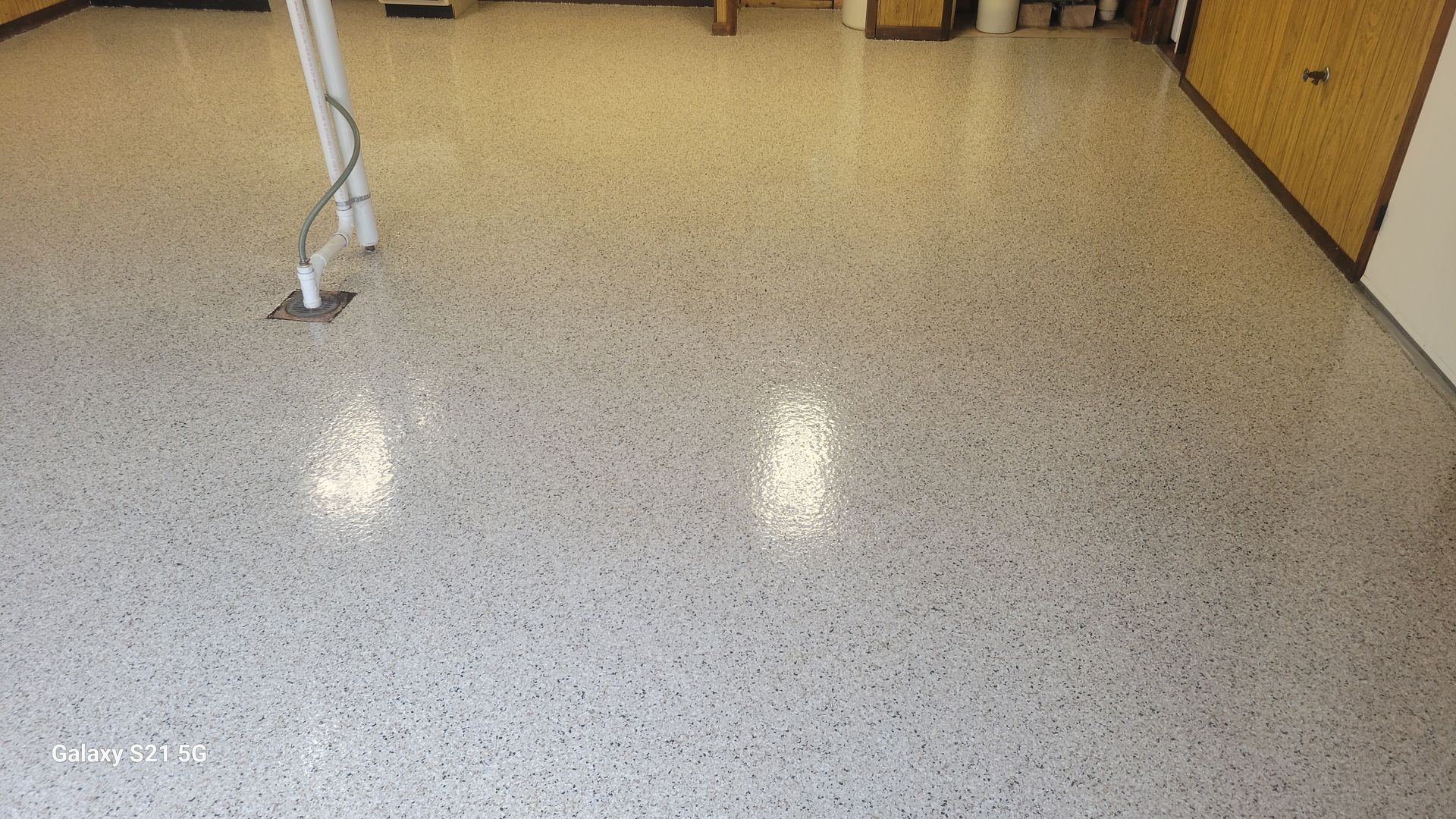 Empty speckled floor in a room with wood cabinets and a visible cable on the left