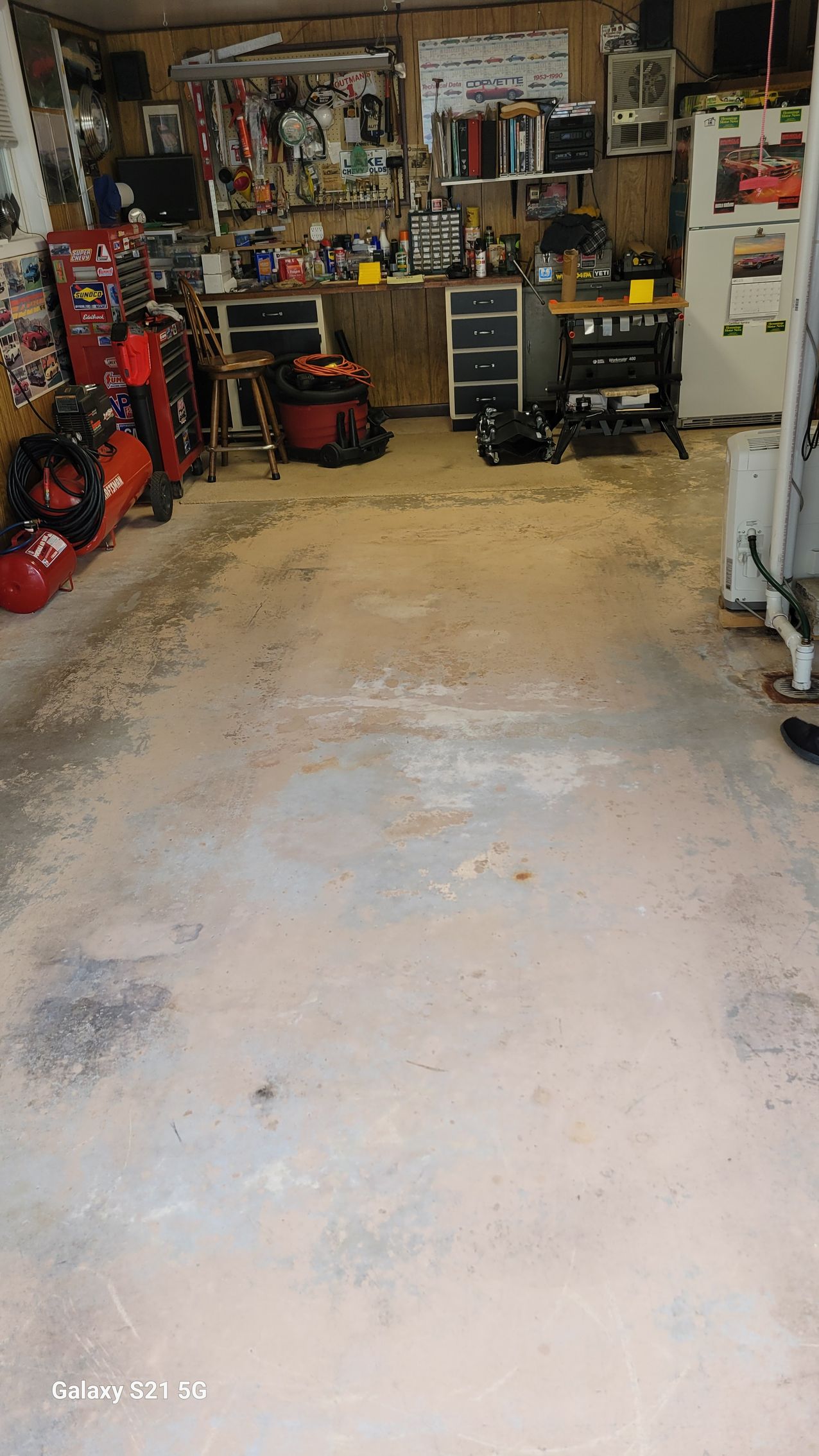 Cluttered garage with tools, shelves, and a stained concrete floor