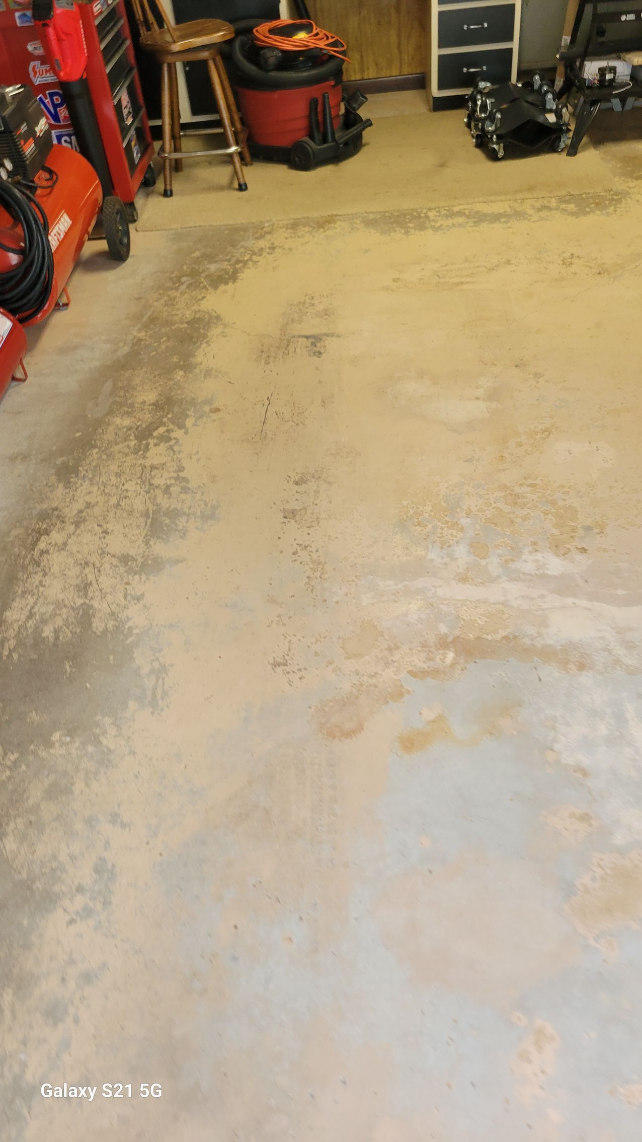 Dirty, stained concrete garage floor with tools and equipment along the walls