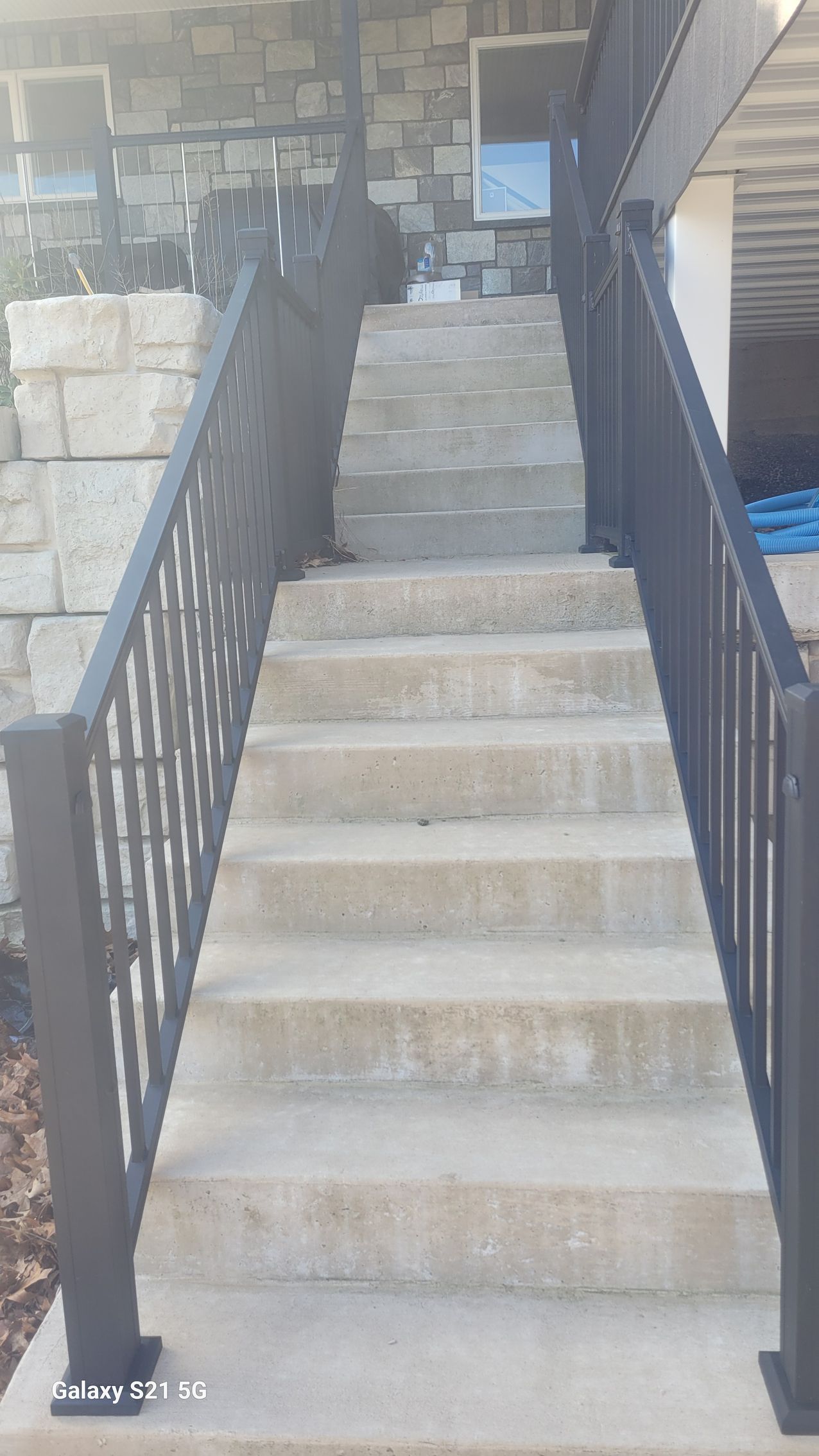 Concrete outdoor staircase with black railings leading up to a landing by a brick building