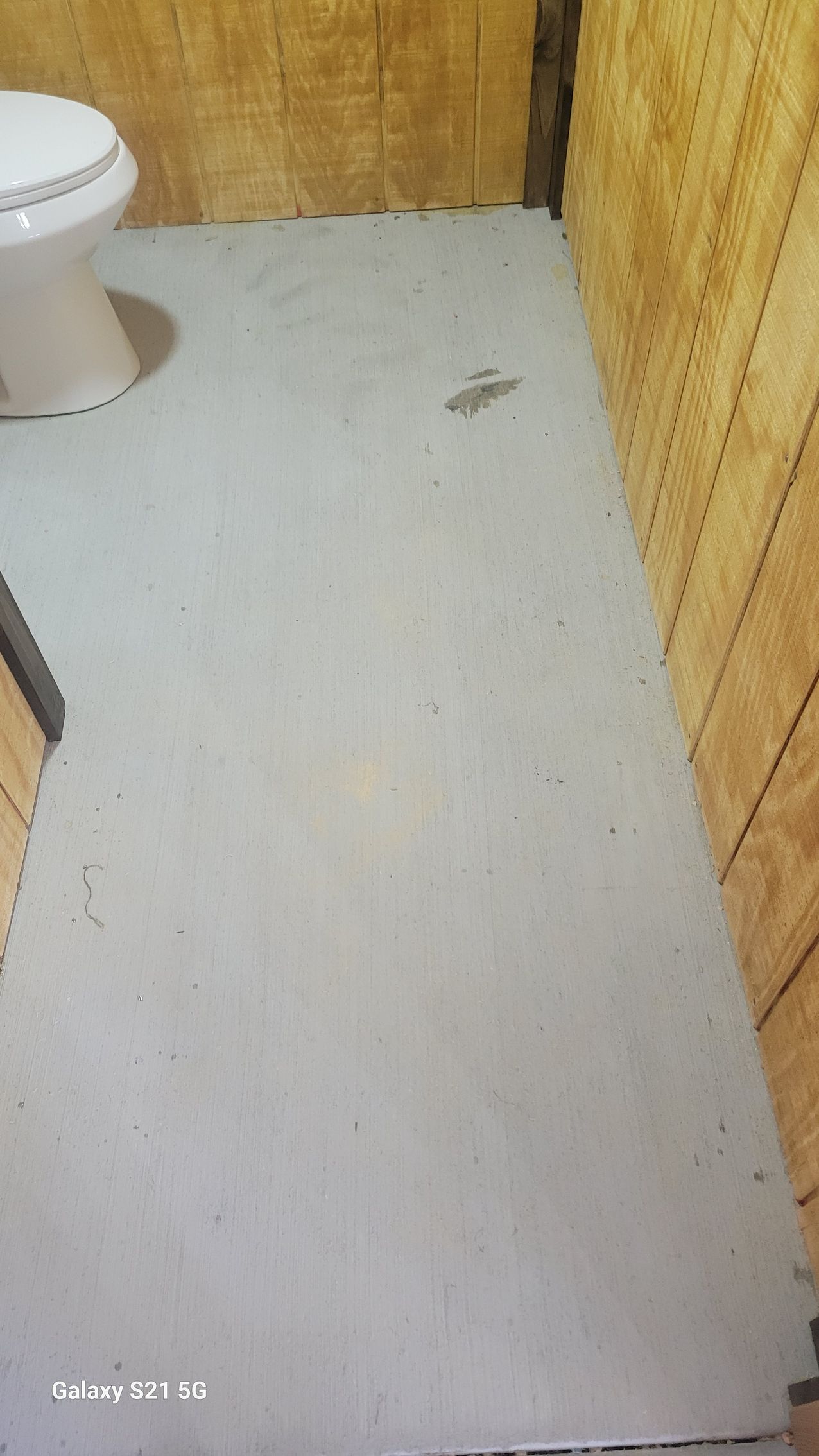 Small bathroom with a white toilet and light floor, showing a few dark stains.