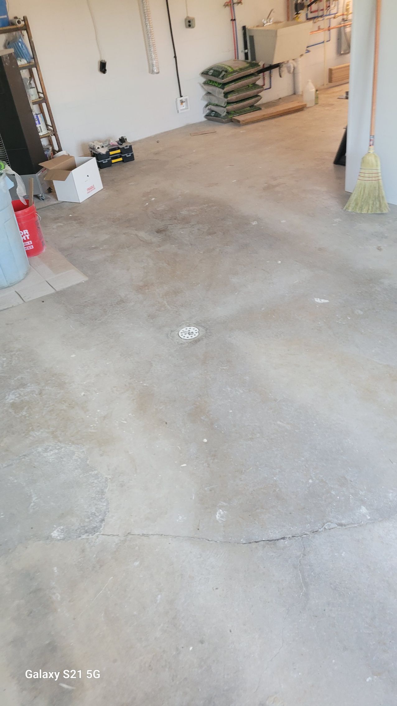Concrete garage floor with a crack, a white door, storage items, and a red fire extinguisher.