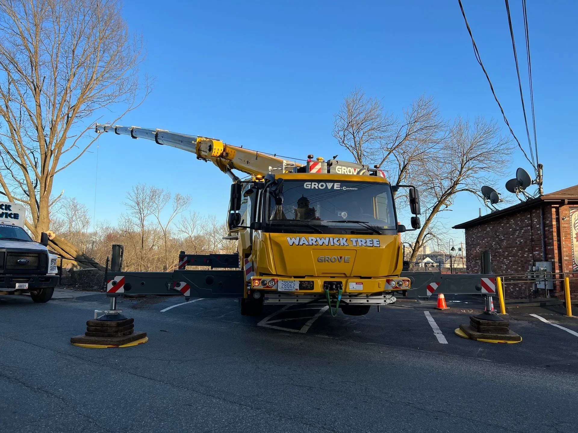 Yellow crane truck on road, boom extended. Barriers and a white truck are visible. Blue sky.