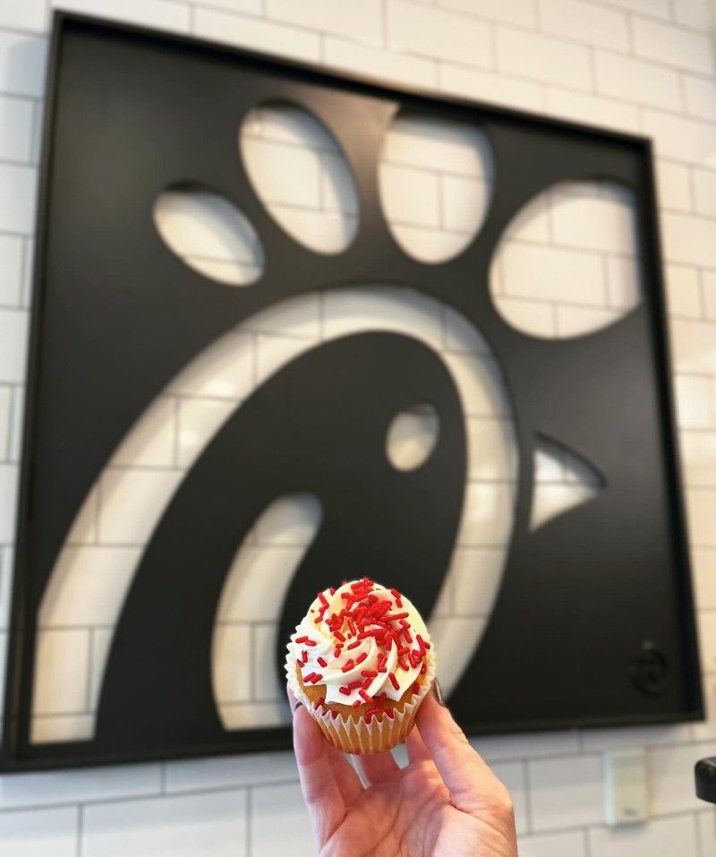 Hand holding cupcake with red sprinkles, in front of a black Chick-fil-A logo.