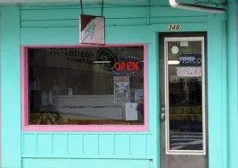 A storefront with a teal exterior, pink window trim, and a door. A window displays an