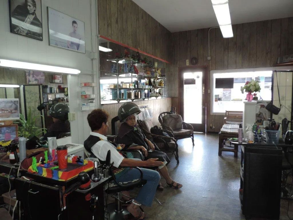 Interior of a small hair salon. Two women sit under hair dryers, and equipment and products are on counters.