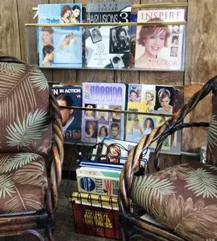 Two chairs with palm-patterned cushions face a magazine rack filled with hair styling magazines.