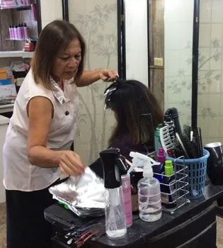 A woman in a salon foil-highlights hair. She is working in front of a mirror, surrounded by styling tools and products.