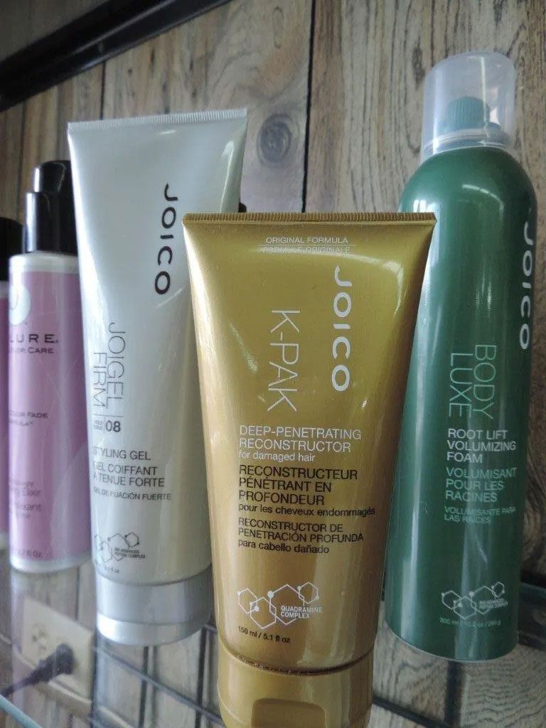 Joico hair product bottles on a shelf. Products include a conditioner, reconstructor, and volumizing mousse.