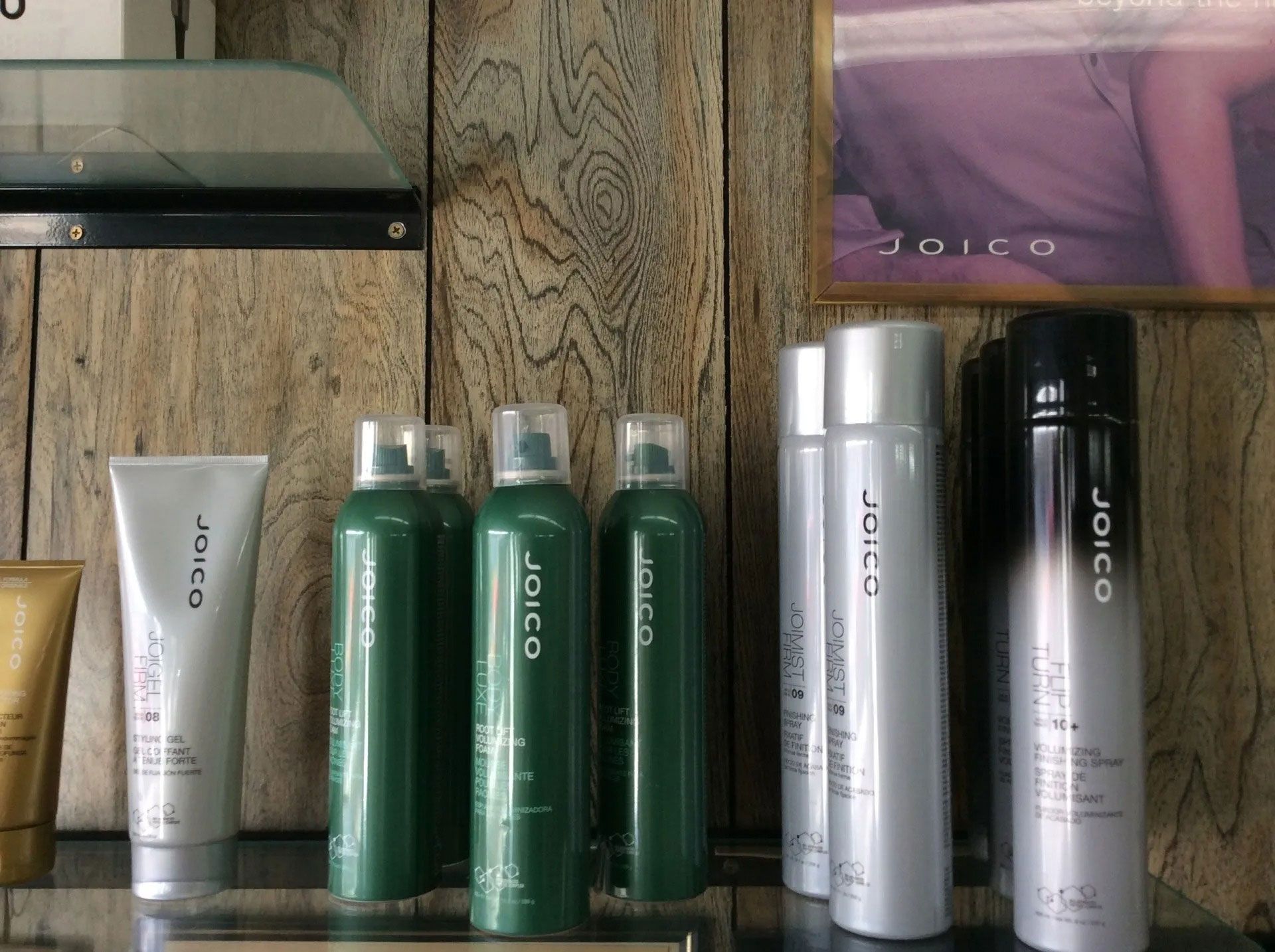 Shelf of Joico hair styling products in silver, green, and black bottles, against a wood-paneled wall.