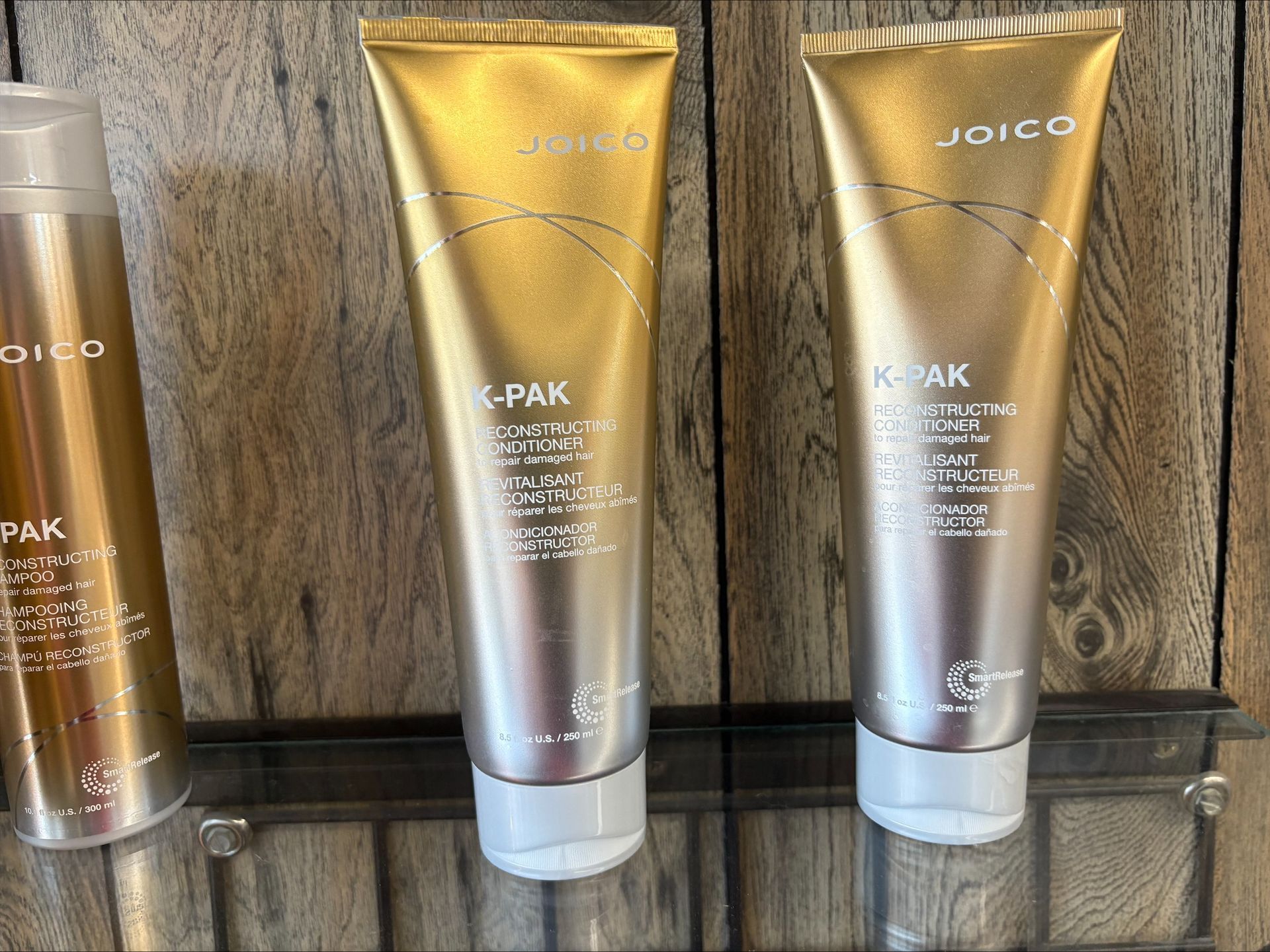 Three gold and silver Joico K-PAK hair products on a shelf against a wood background.