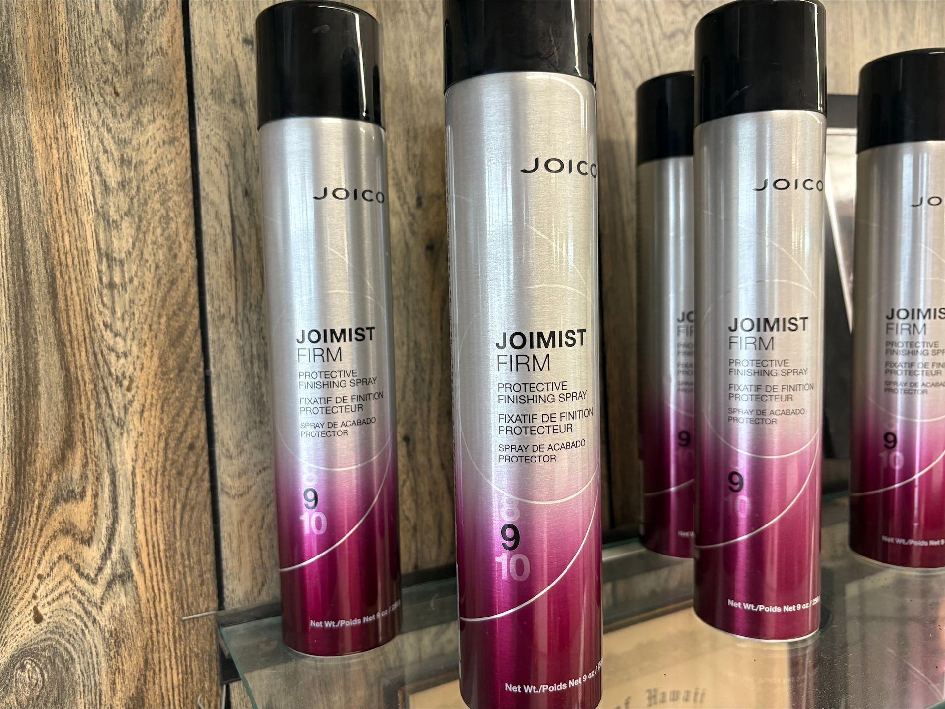 Rows of Joico hairspray cans on a shelf, silver and pink labels, black caps, and the word