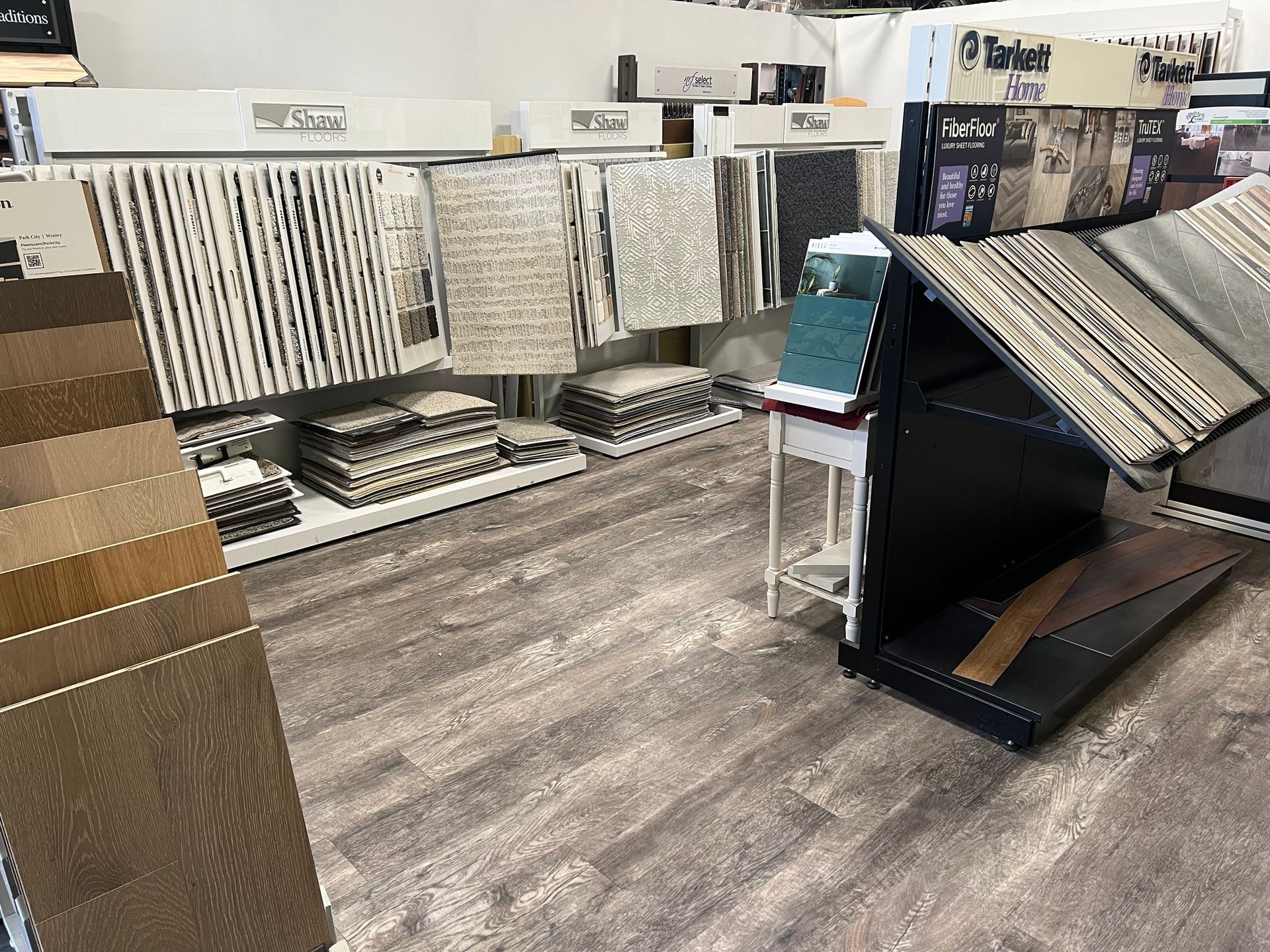 A showroom with flooring samples, including wood and carpet. Display racks with samples on a wood-look floor.