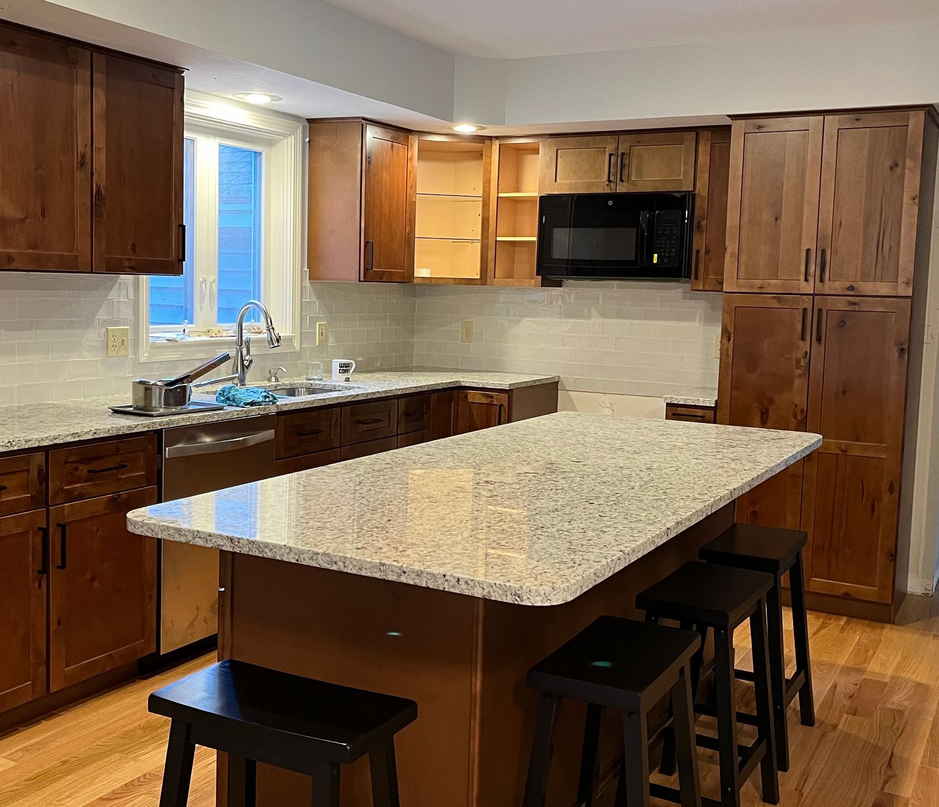 Kitchen with brown cabinets, granite countertops, and a central island with bar stools.