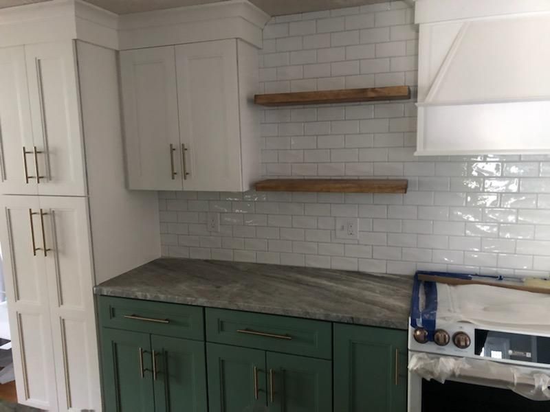 Kitchen with white cabinets, green lower cabinets, wood shelves, and white subway tile backsplash.
