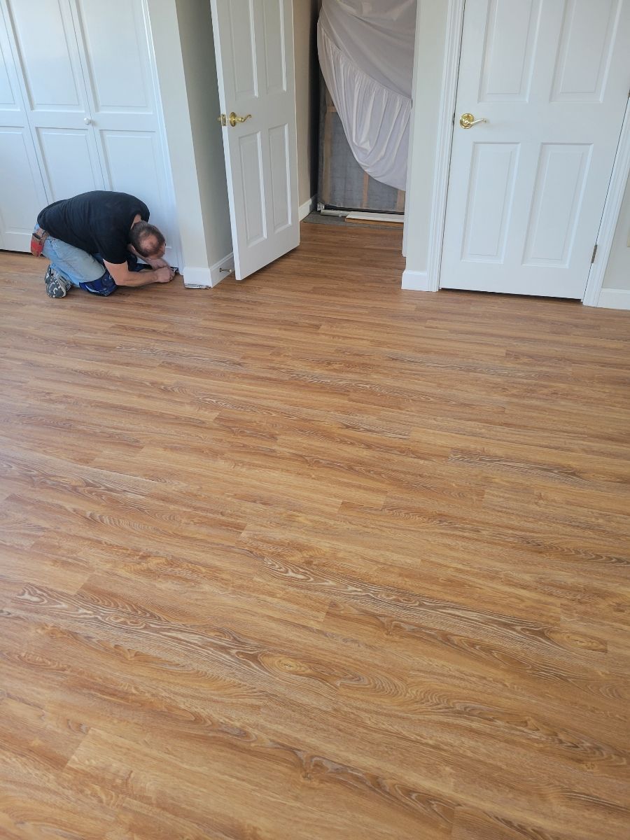 Person kneeling, installing brown wood-look flooring near white doors in a room.