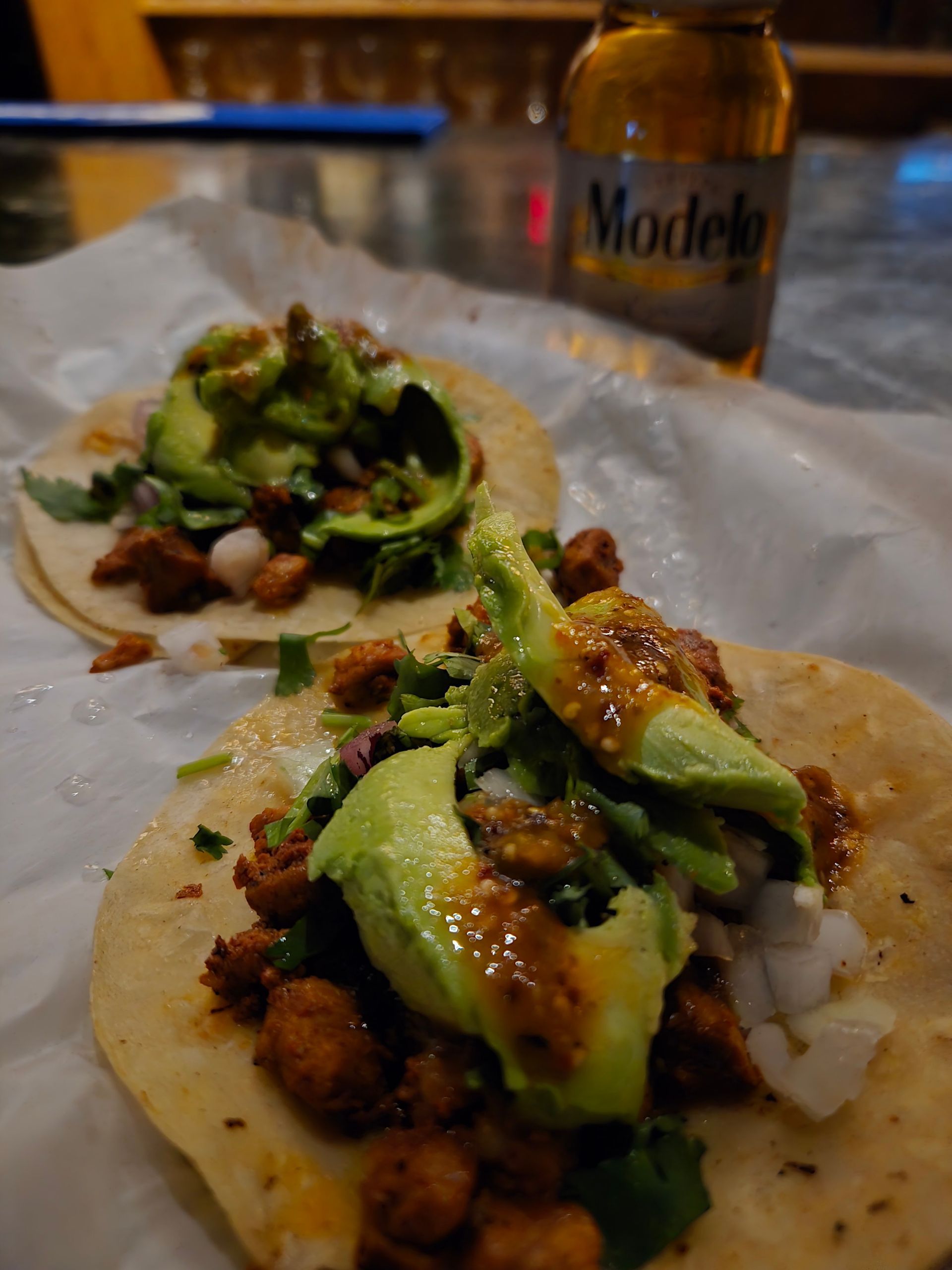 Two tacos are sitting on a table next to a bottle of modelo beer.