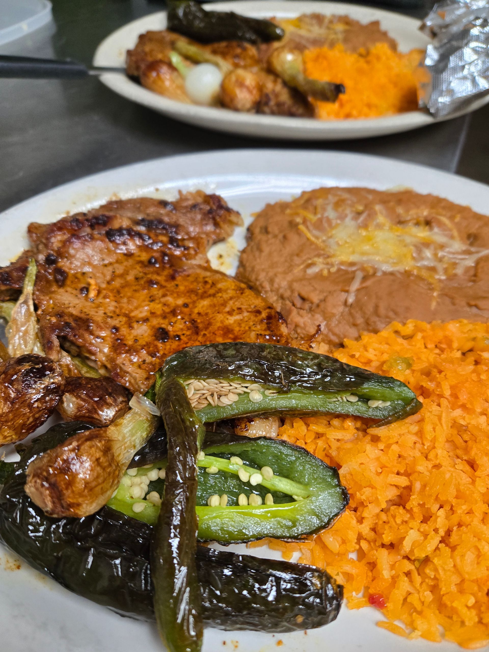 A white plate topped with meat , rice , beans and peppers.