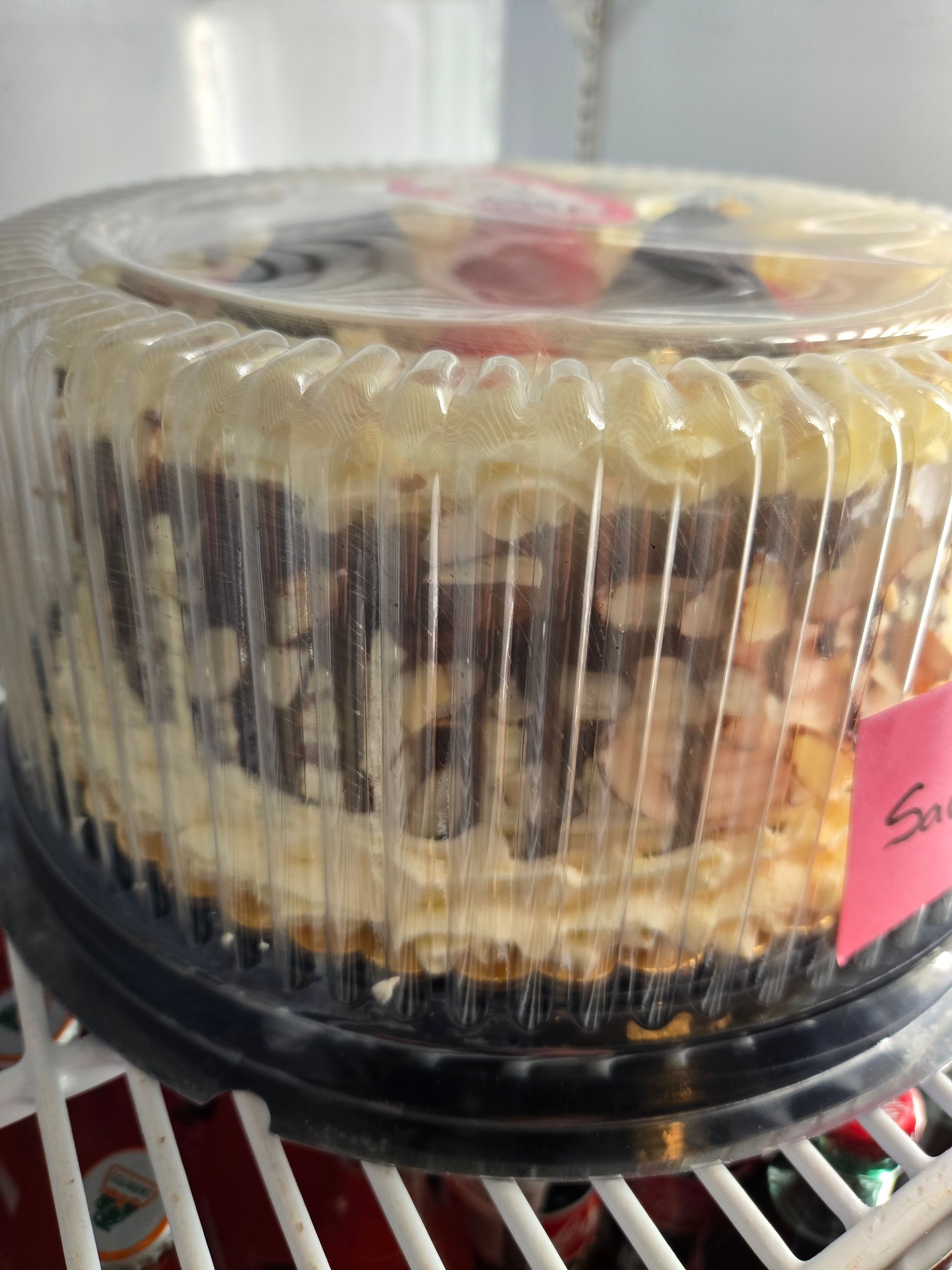 A cake in a plastic container with a pink tag that says ' strawberry ' on it
