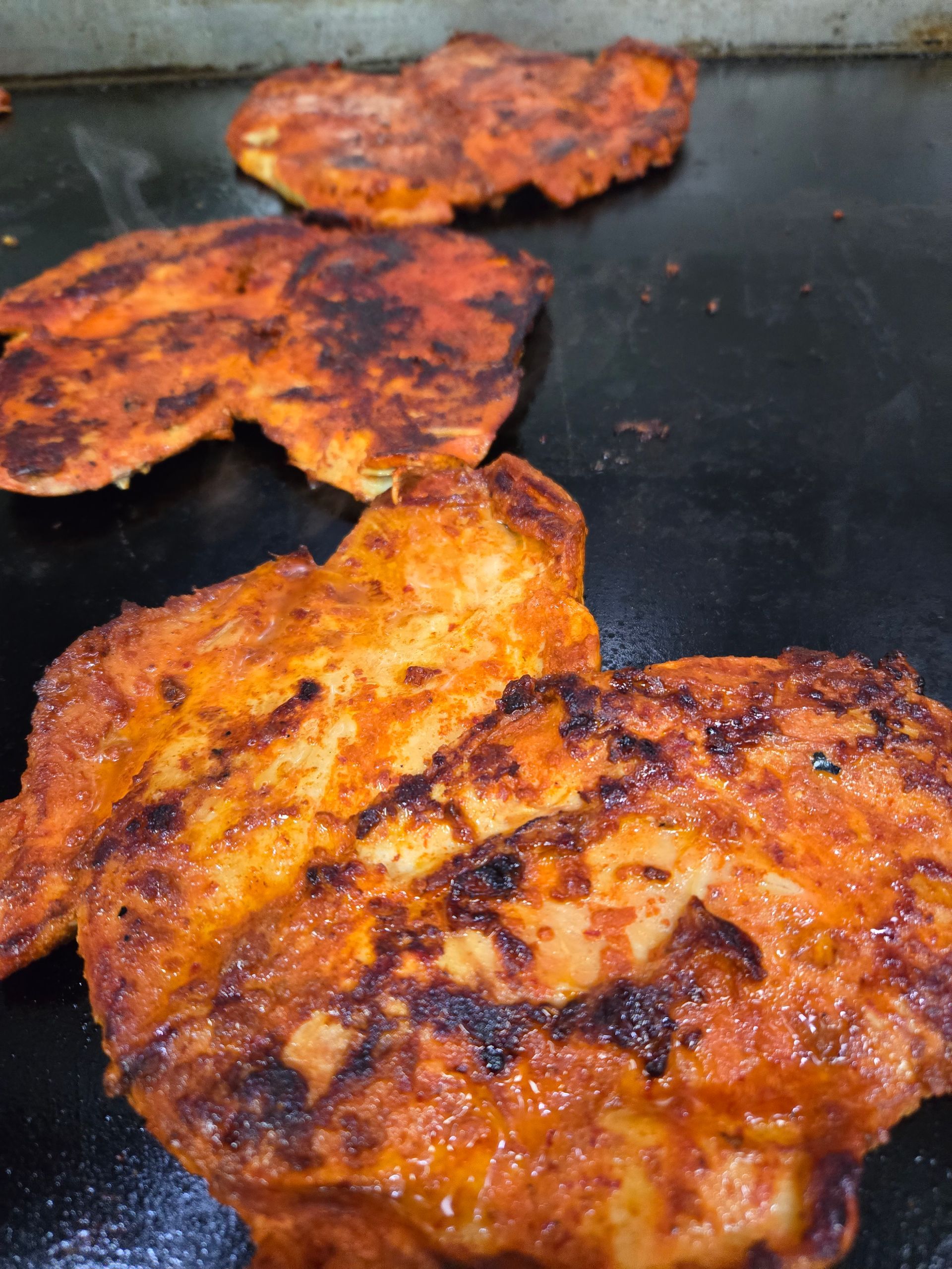 Three pieces of chicken are cooking on a grill.