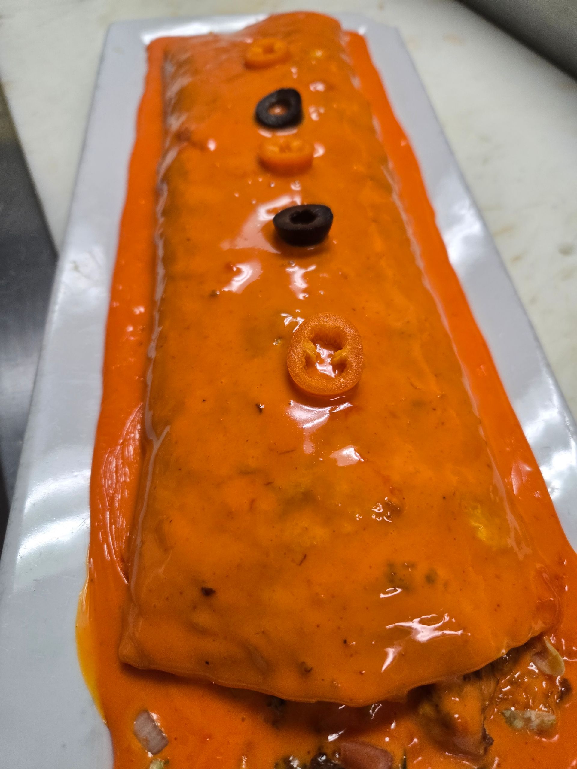 A burrito with sauce and olives on a white plate